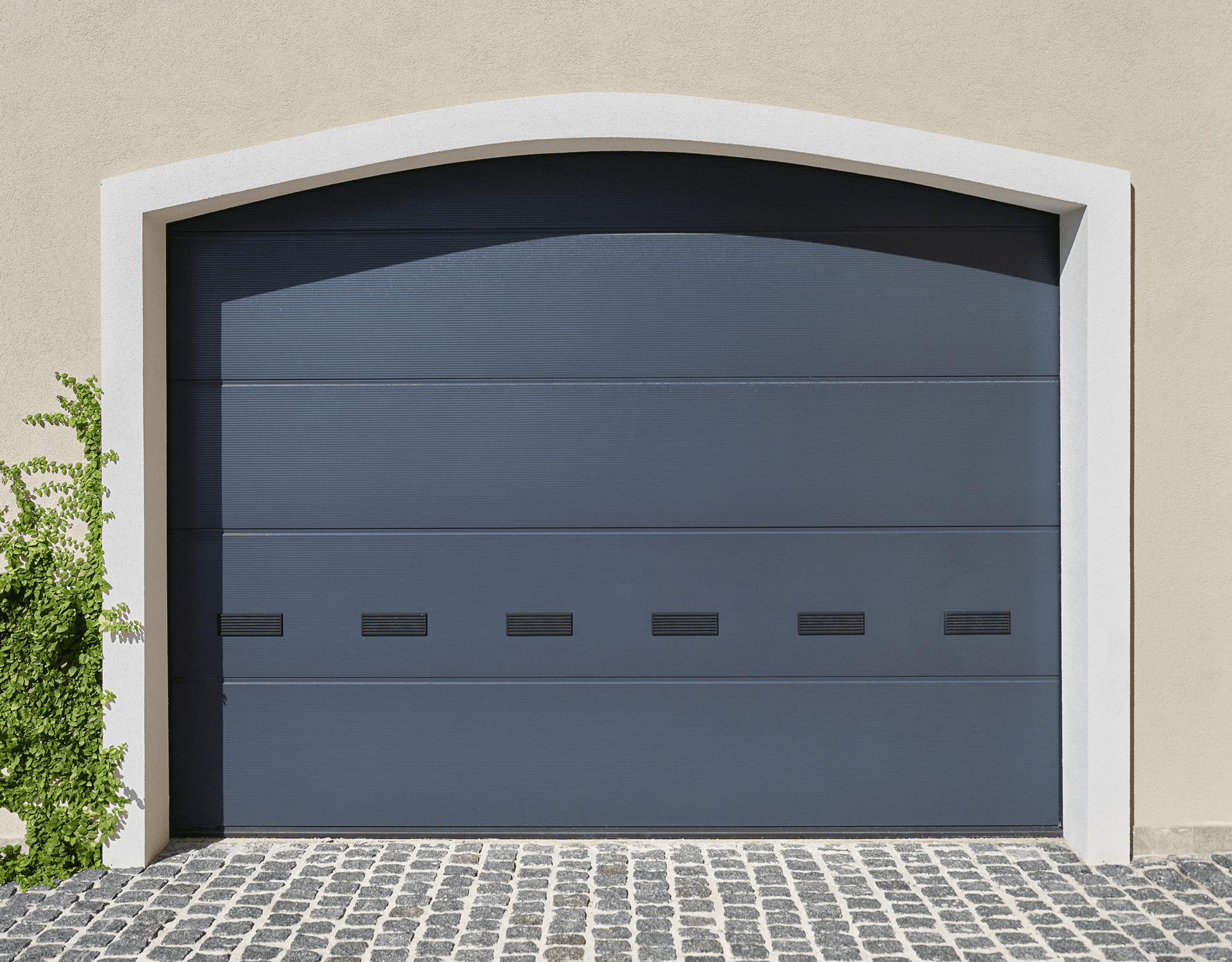 Modern dark gray garage door with frosted windows on a cobblestone driveway.